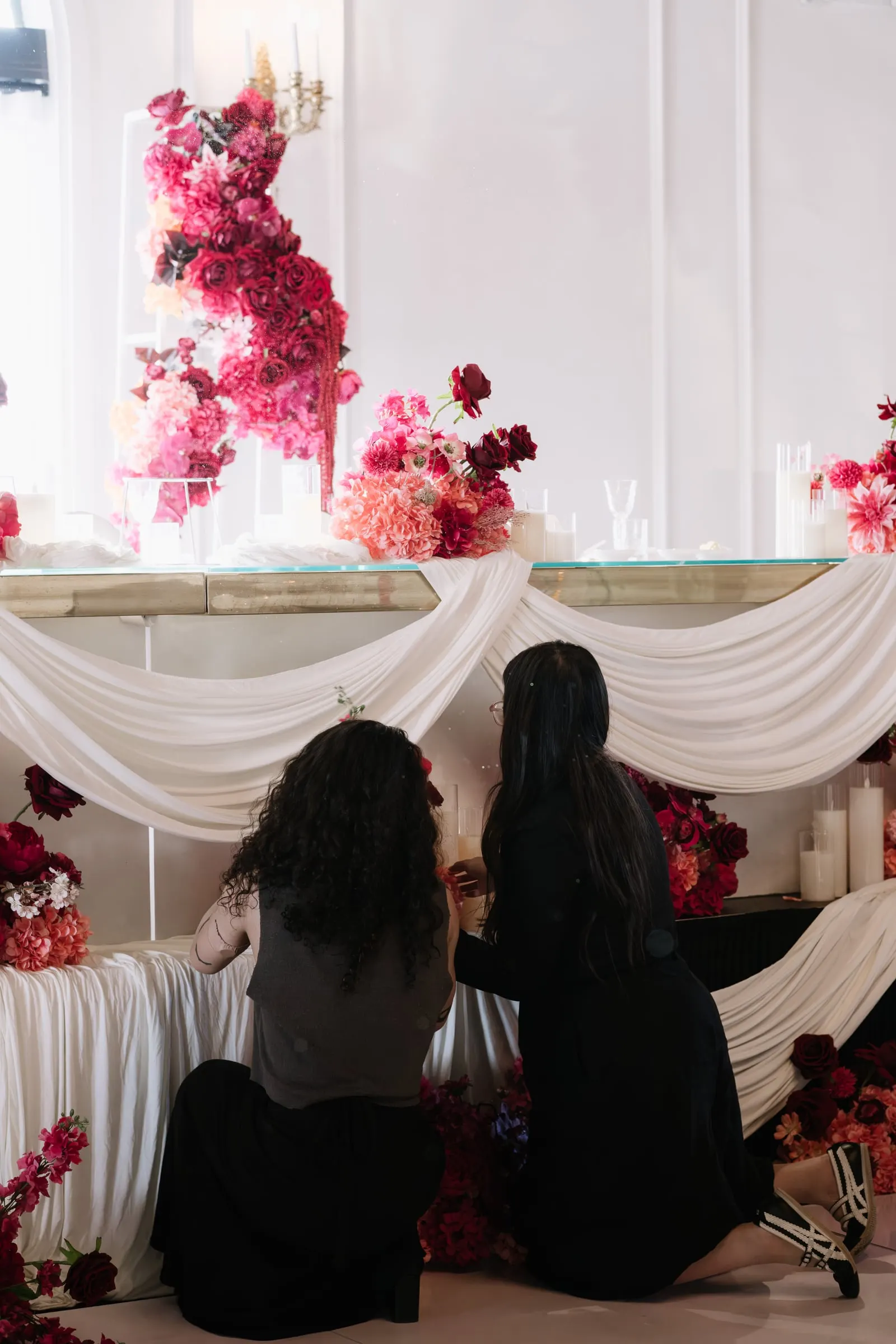 Two of the Last August Events team styling a white draped backdrop with pink and red florals