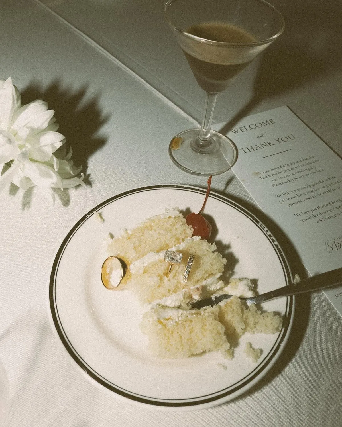 Slice of wedding cake on a glass plate beside a cocktail and menu card