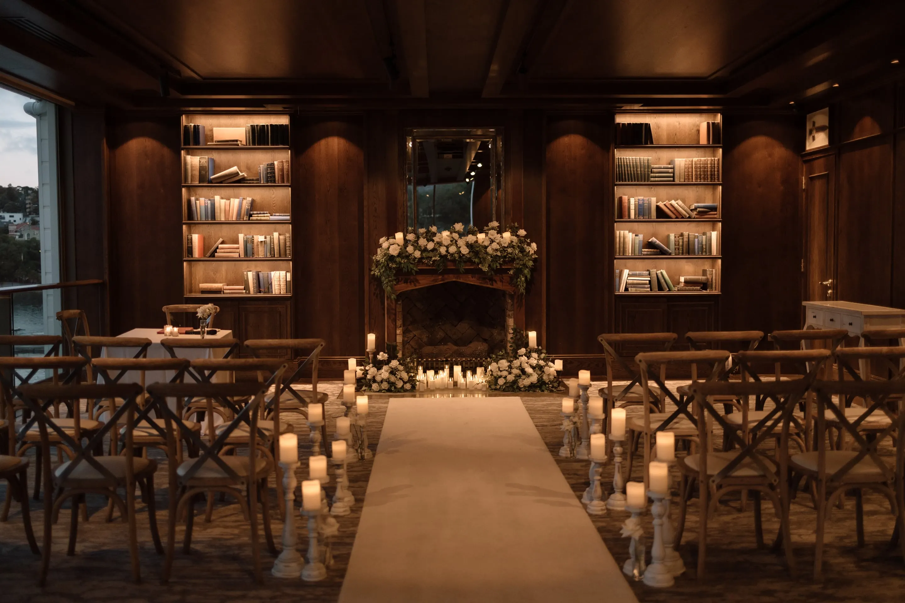 Candlelit ceremony aisle in a library room, with florals at the fireplace