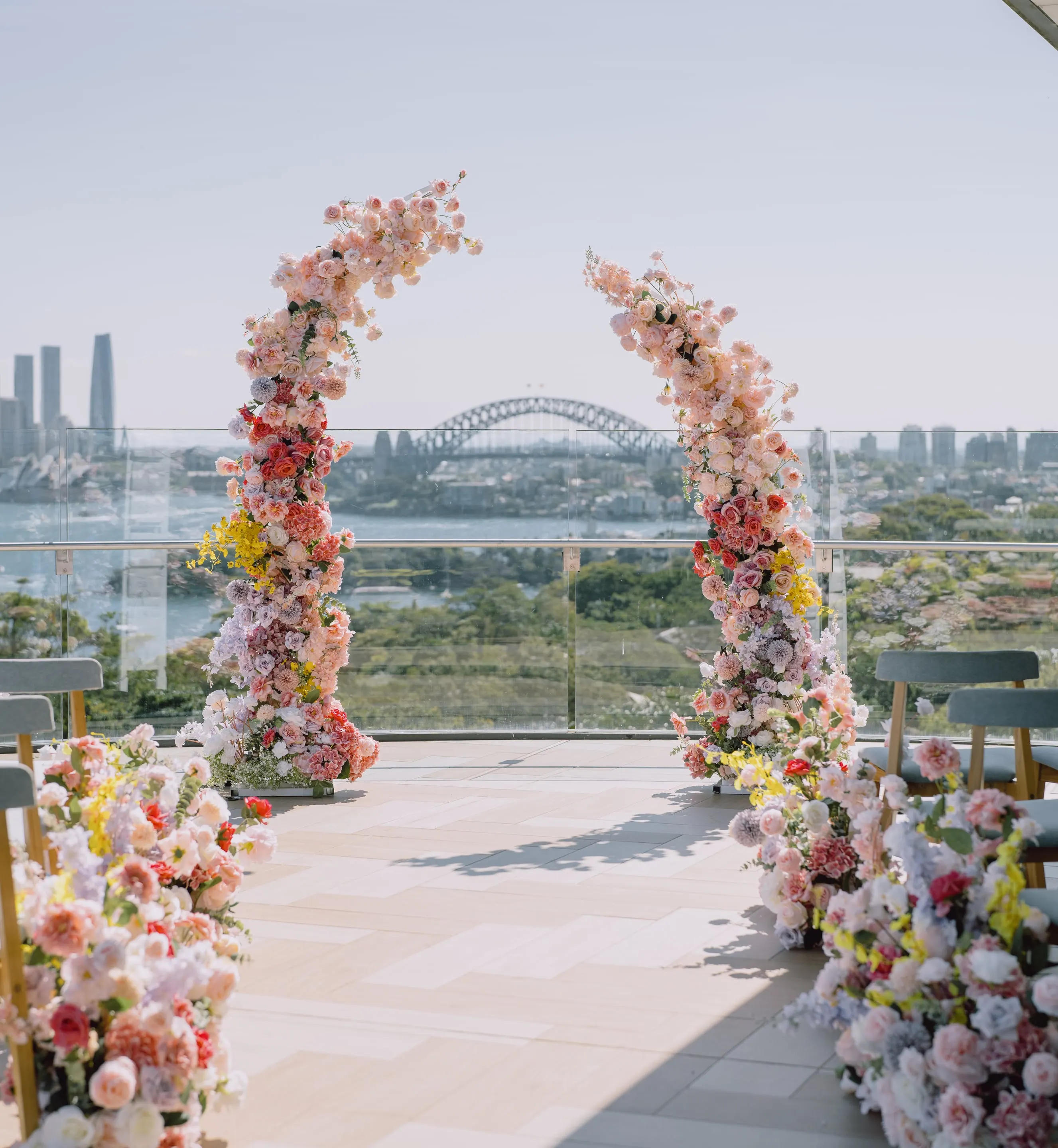 Floral half-arches on either side of the aisle on a harbourside terrace, with the city skyline behind
