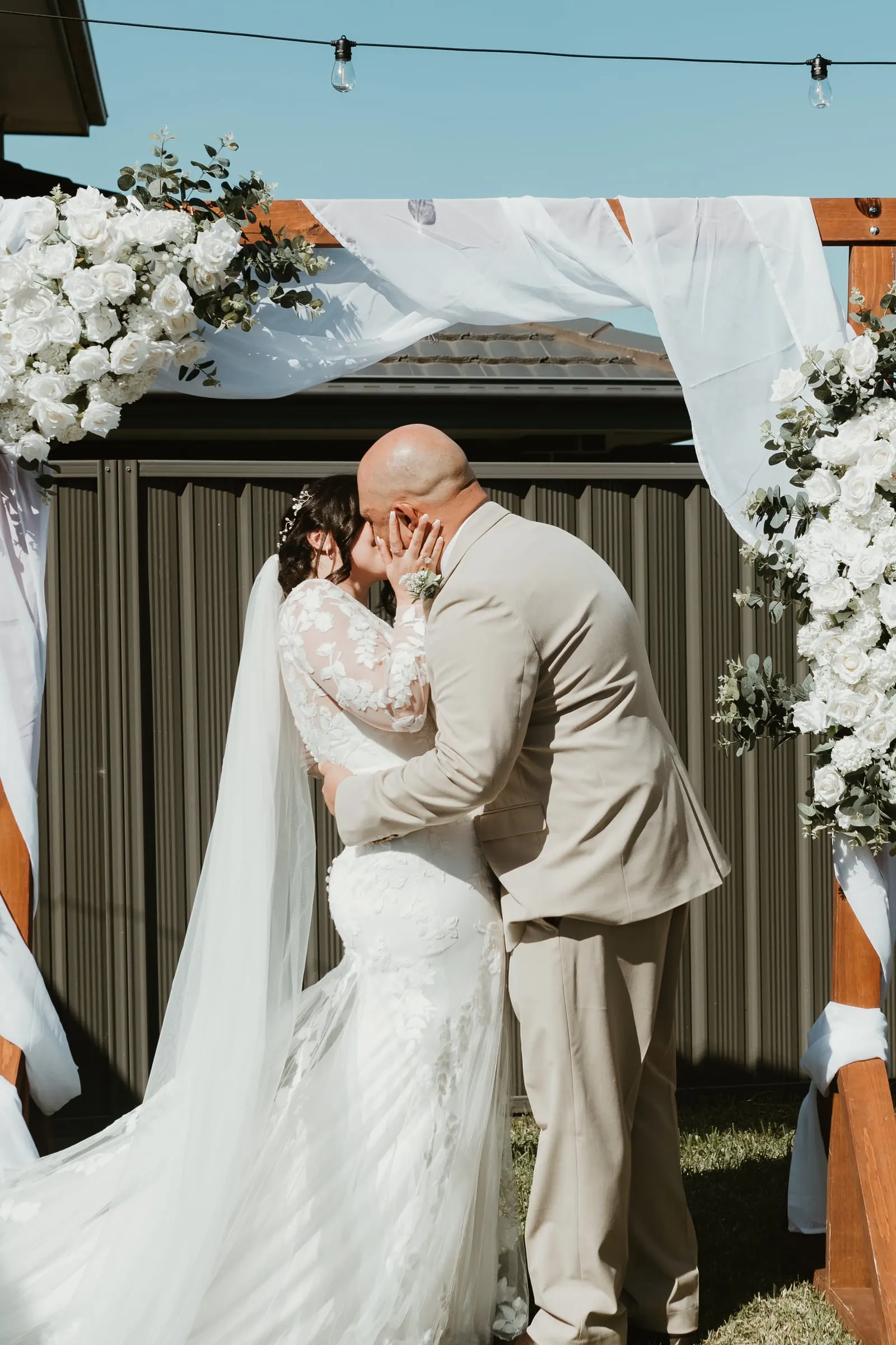Bride and groom kissing beneath a white floral arch