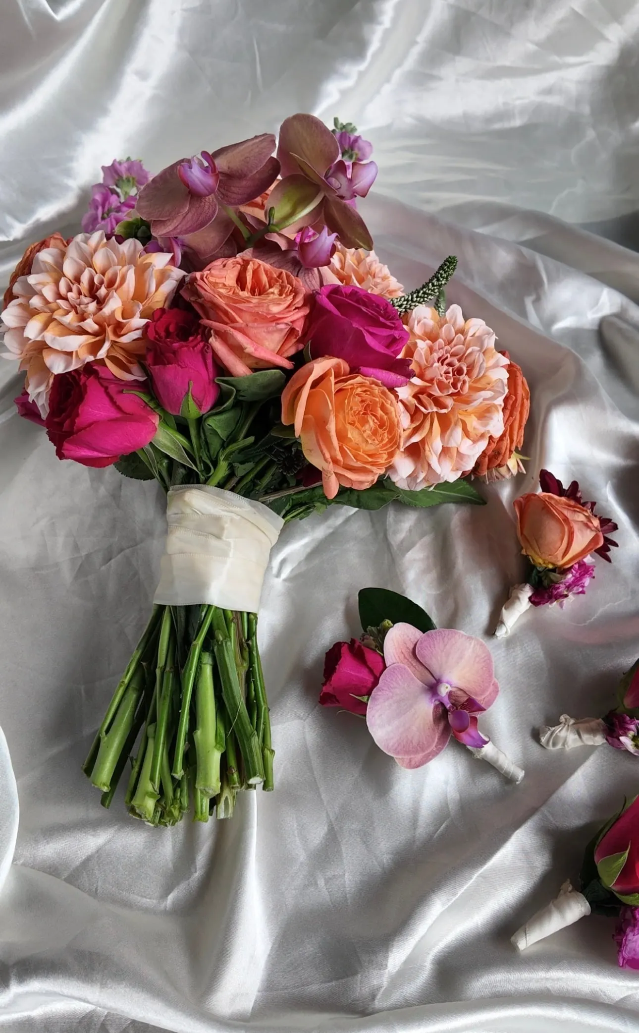 Bridal bouquet of pink, peach and burgundy roses resting on white satin