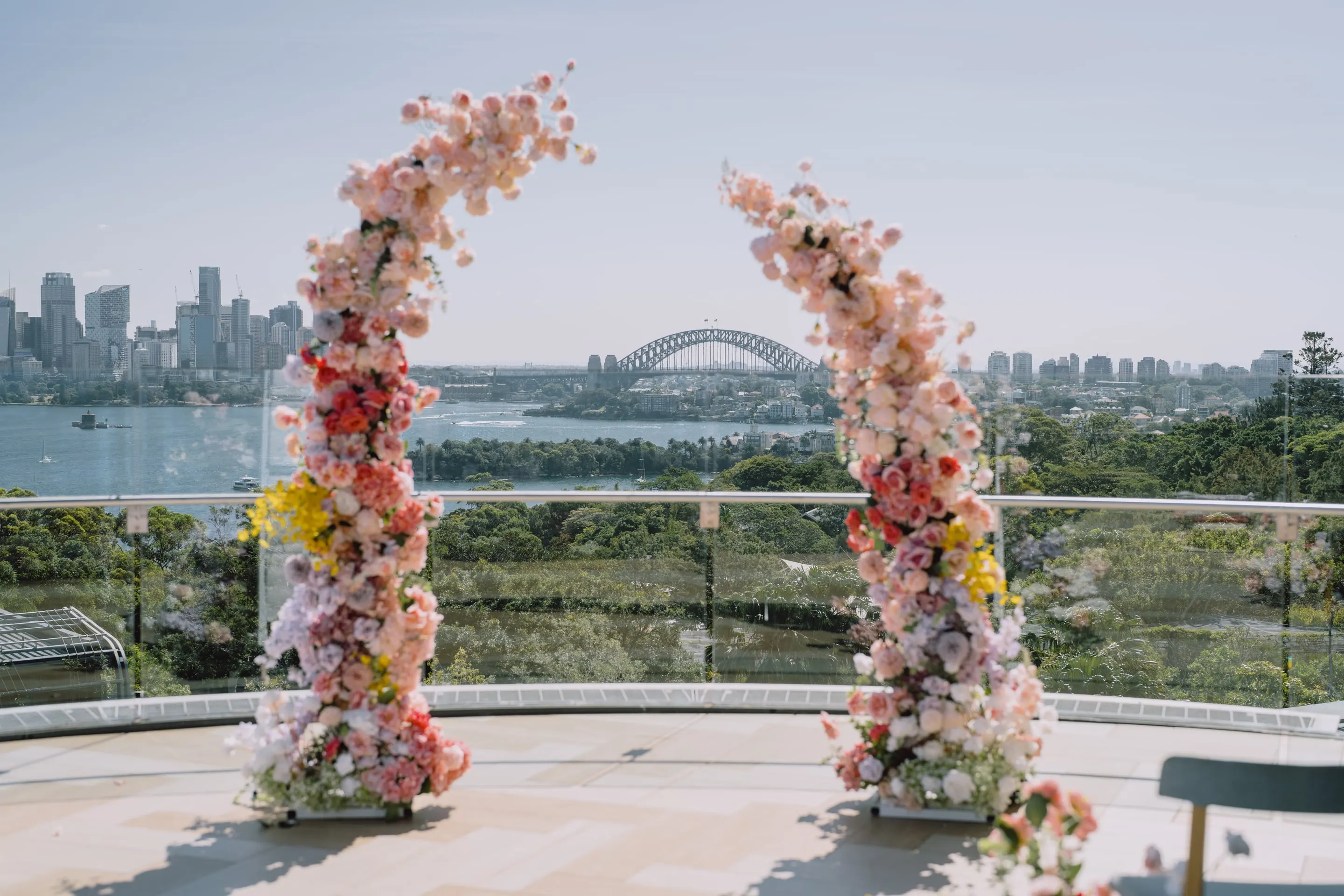 Pastel floral half-arches on a harbourside terrace framing the Sydney Harbour Bridge