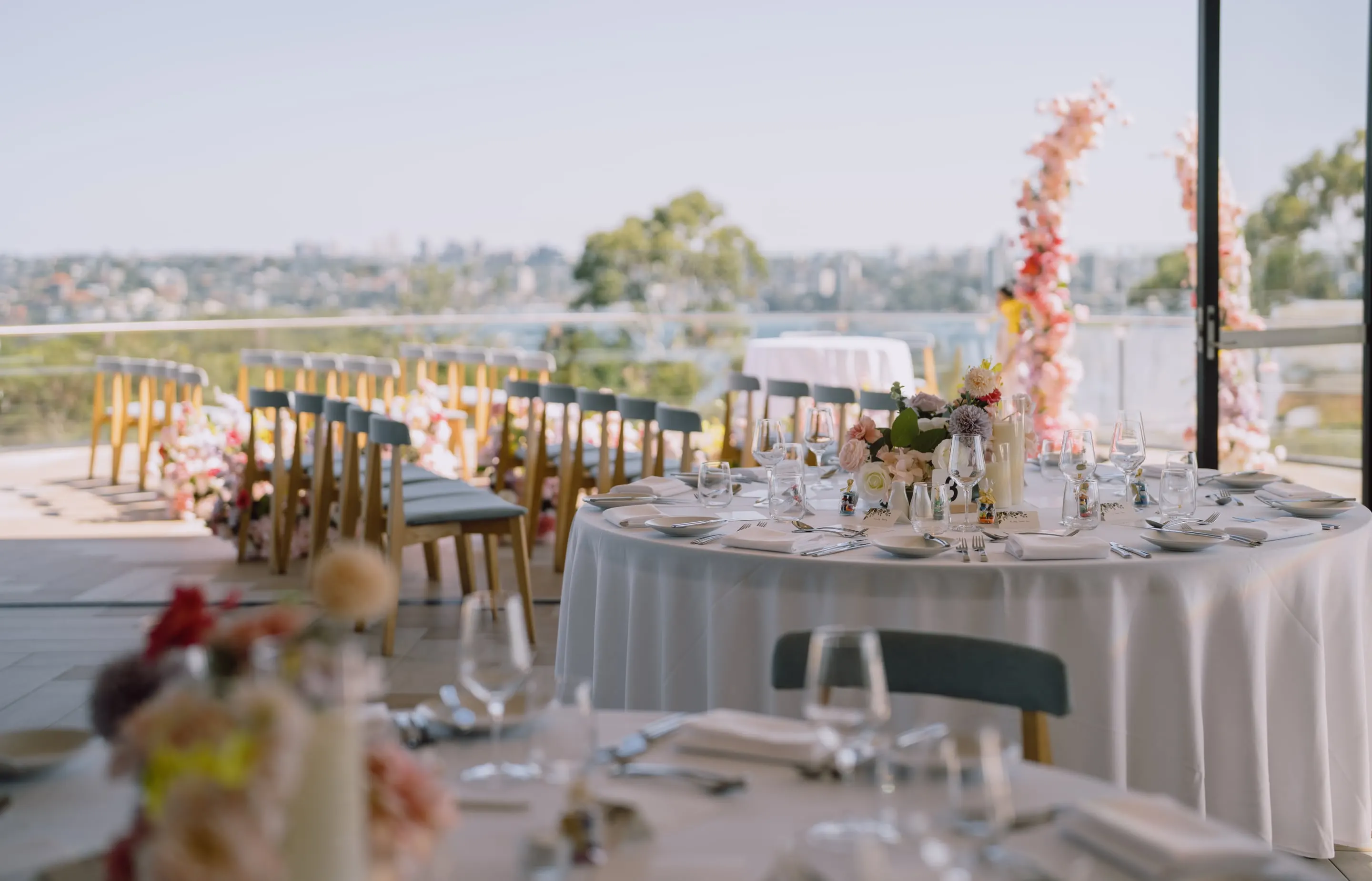 Reception tables with pastel centrepieces on a terrace overlooking the harbour, ceremony arches beyond