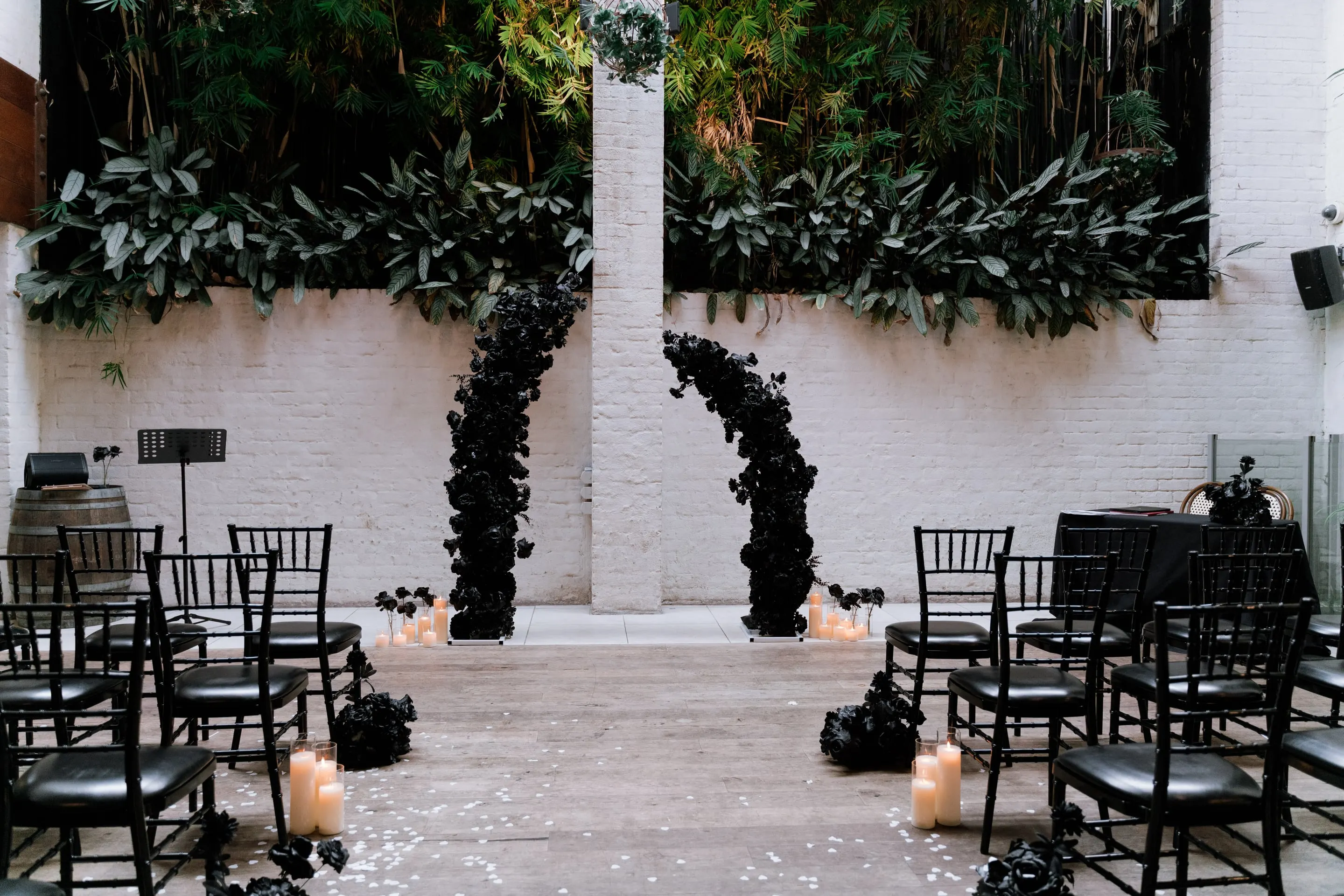 Courtyard ceremony with black floral arches, black chairs and candles against a white brick wall and greenery