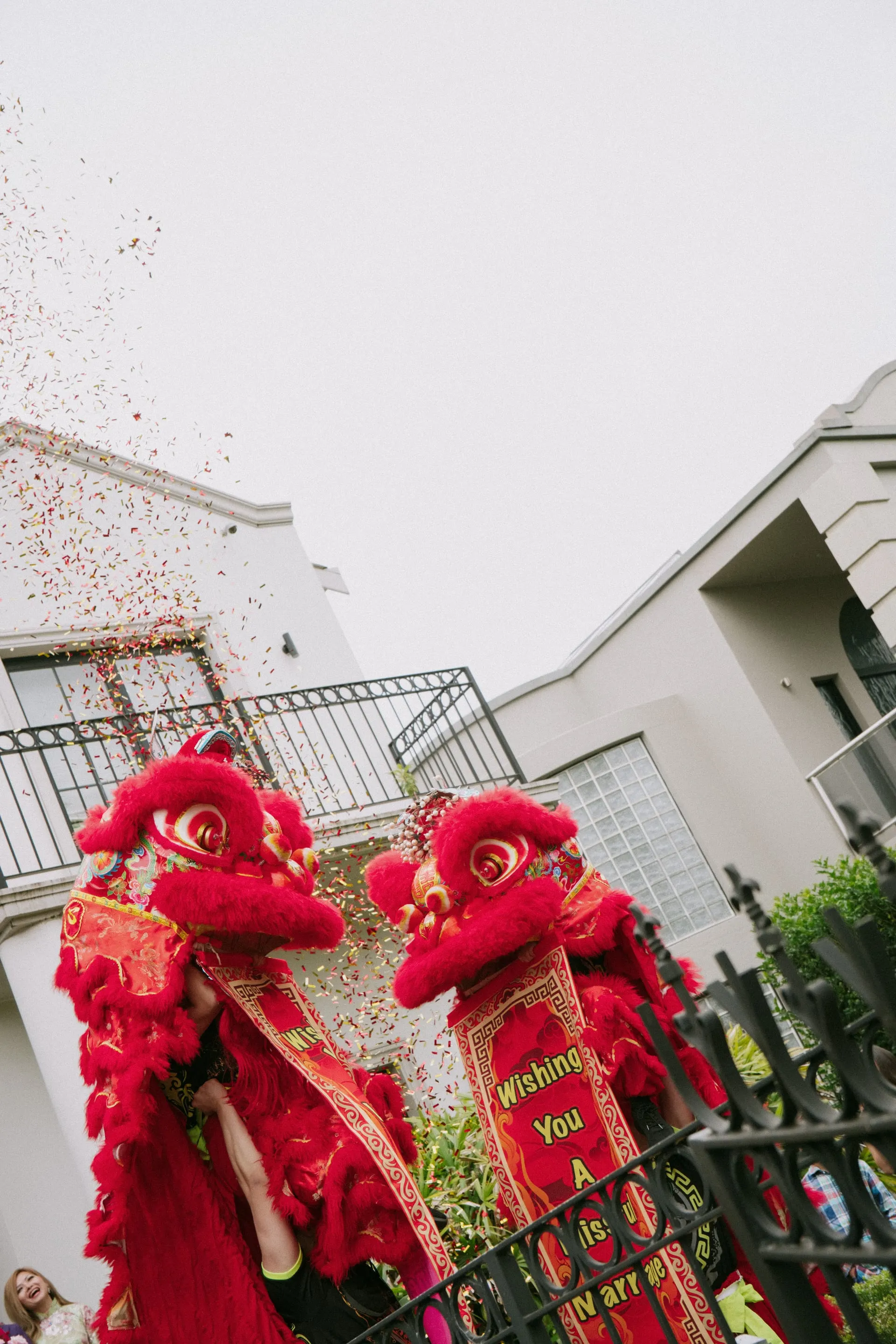 Two red lion dancers under a shower of confetti outside the family home on the tea ceremony morning