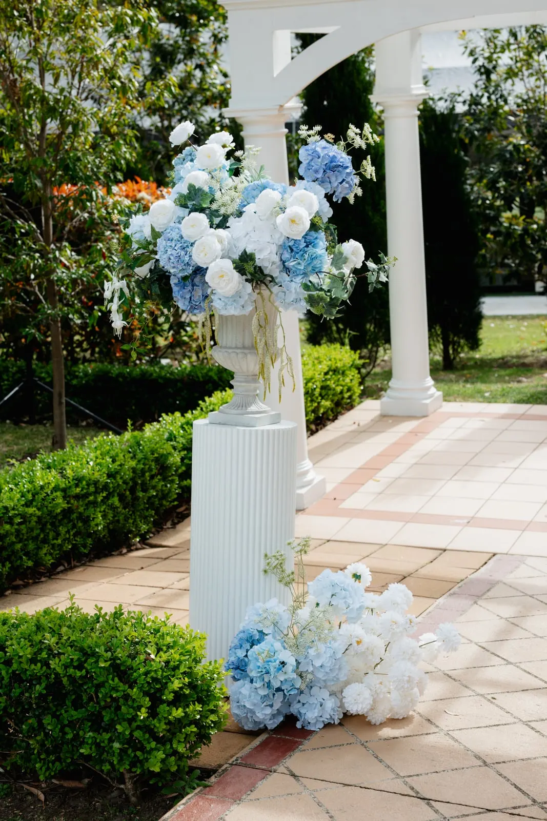 Low white floral arrangements lining a ceremony aisle beside white columns