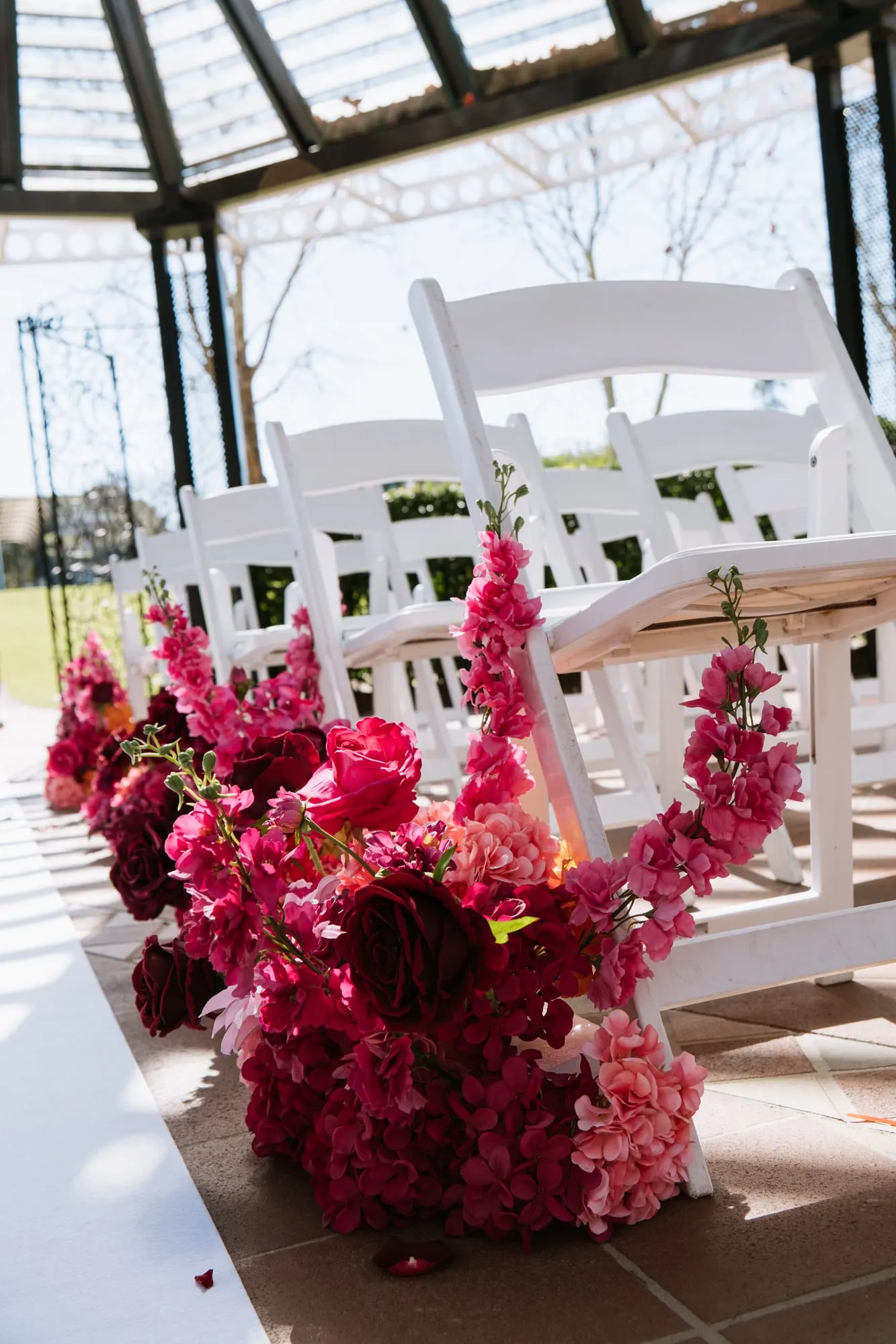 Red and pink floral arrangement at the end of a row of white ceremony chairs