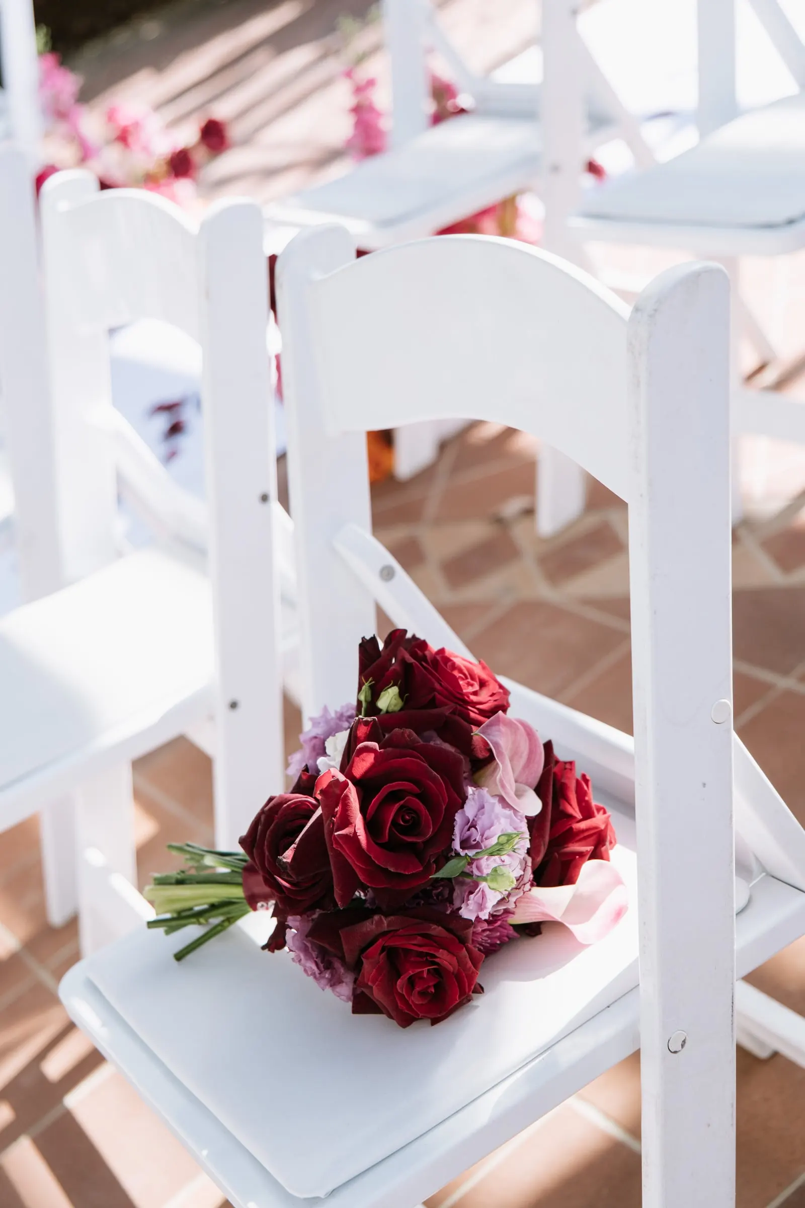 Bridal bouquet of deep red roses and pink orchids resting on a white chair