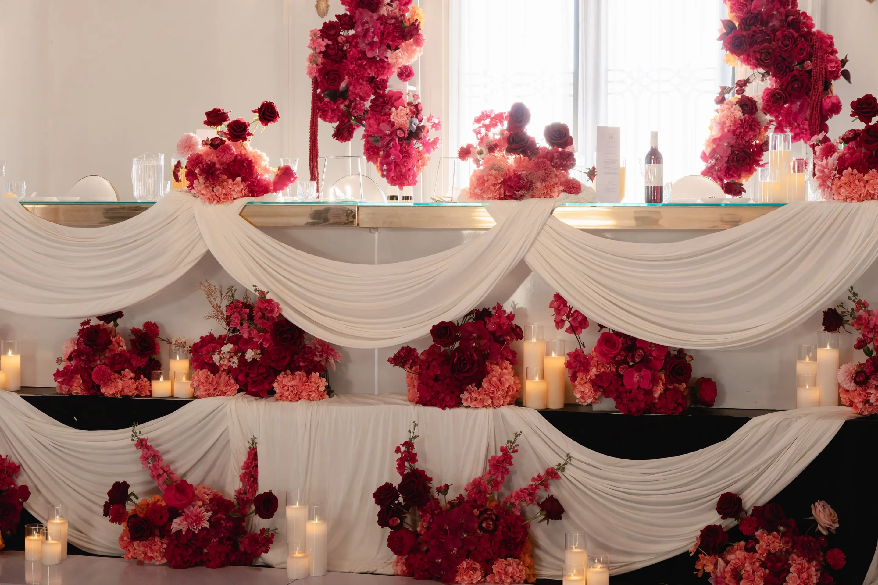 Long bridal table with white swags, red and pink floral installations and pillar candles