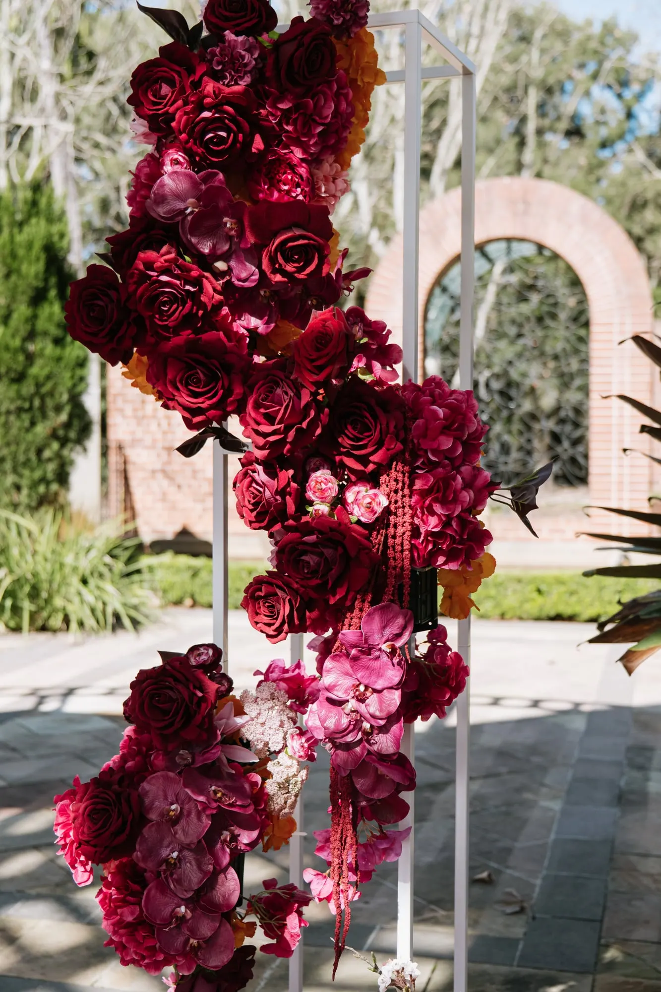 Floral column of deep red roses and pink orchids beside the ceremony aisle