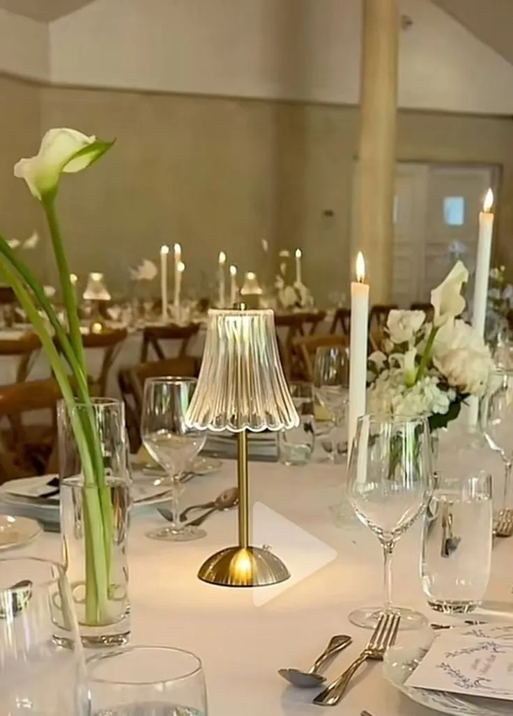 Gold table lamp with a ribbed glass shade beside a calla lily on a set table