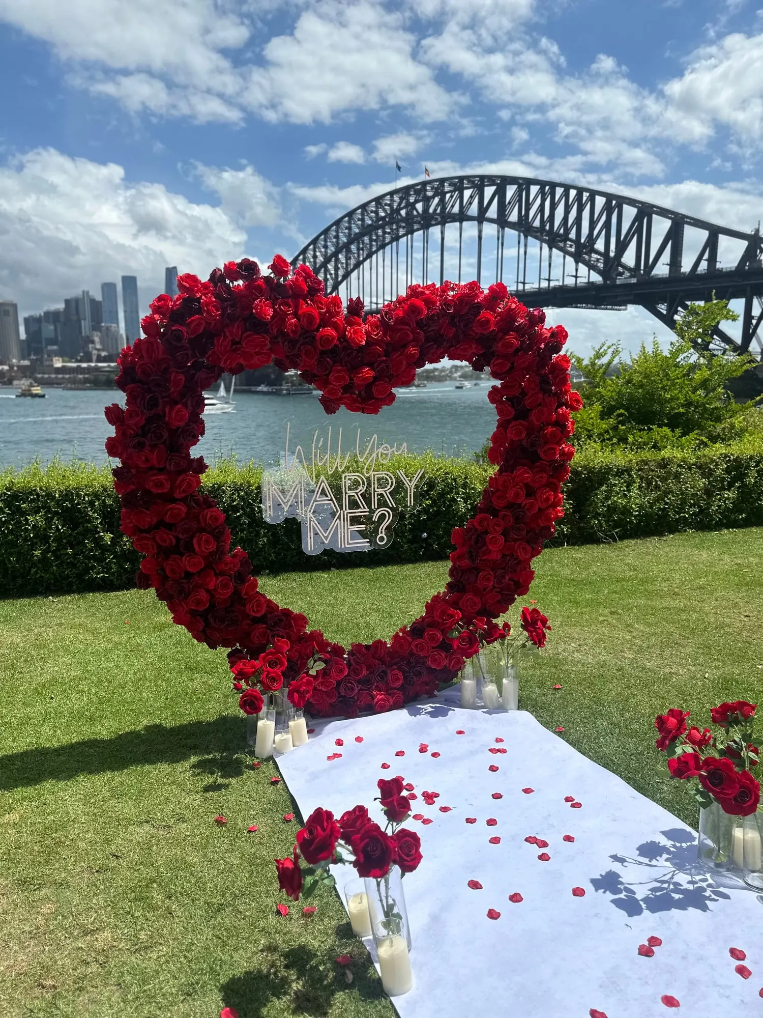 Red rose heart arch and candlelit aisle runner set up on a harbourside lawn