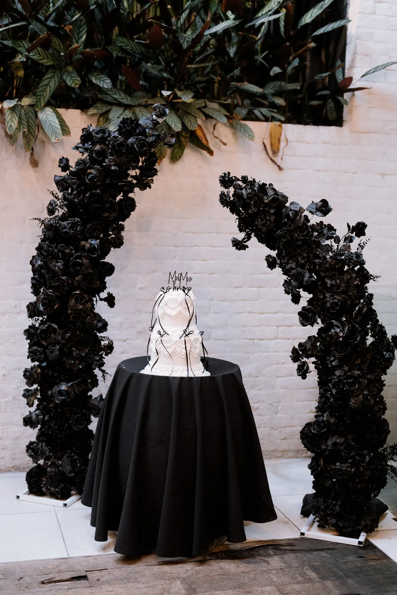 Black floral arch framing a cake on a black-draped table