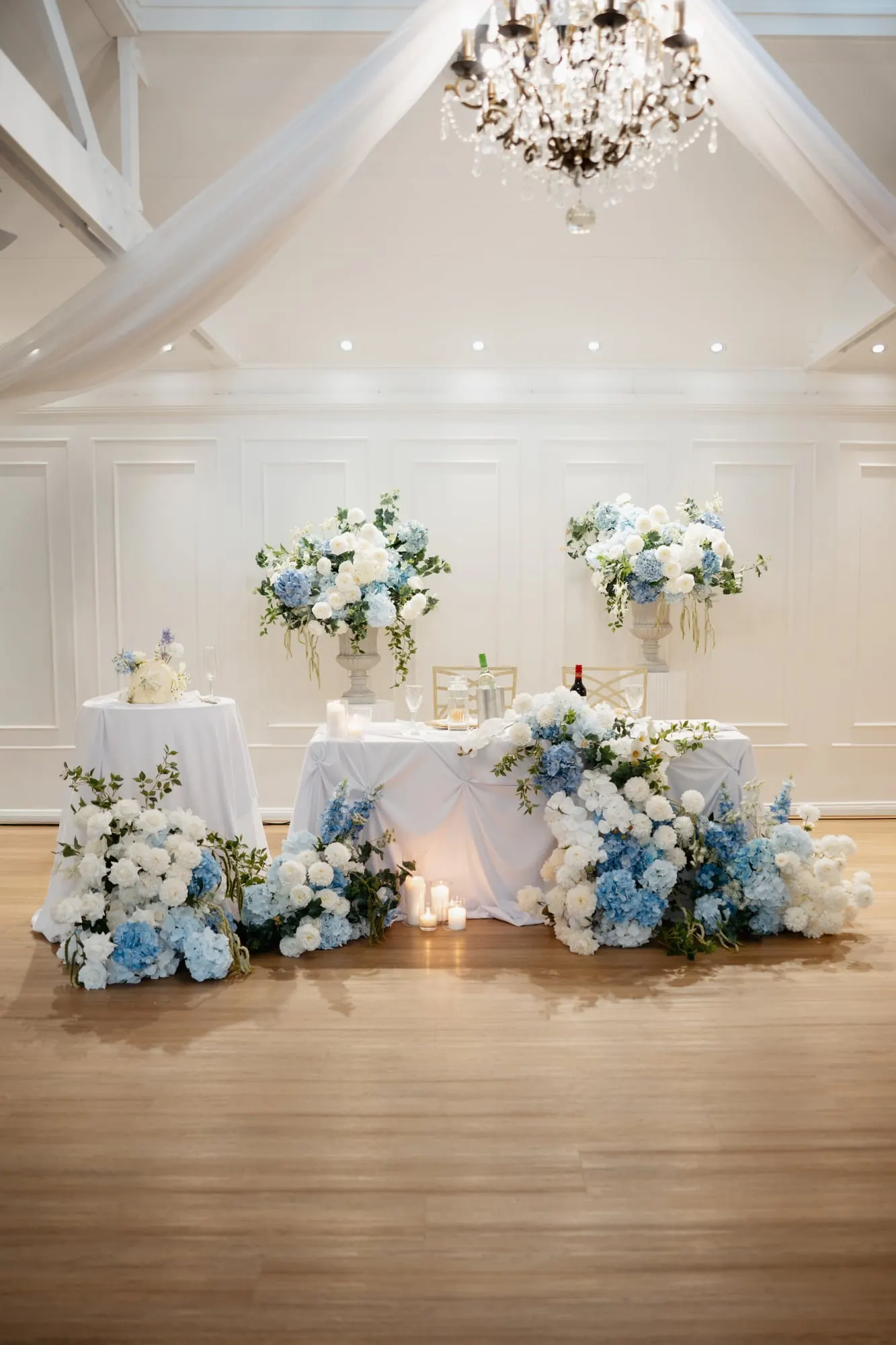 Sweetheart table with white and blue florals beneath a chandelier