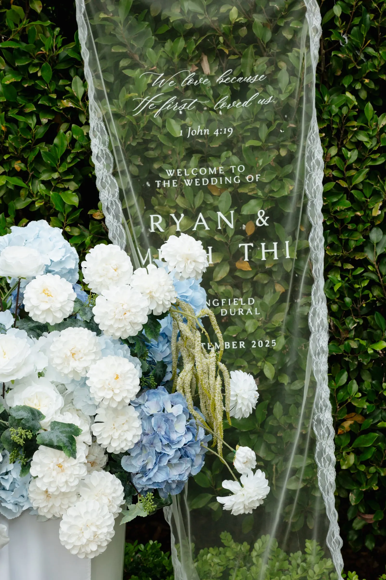 Clear acrylic welcome sign with white lettering, framed by blue and white hydrangeas