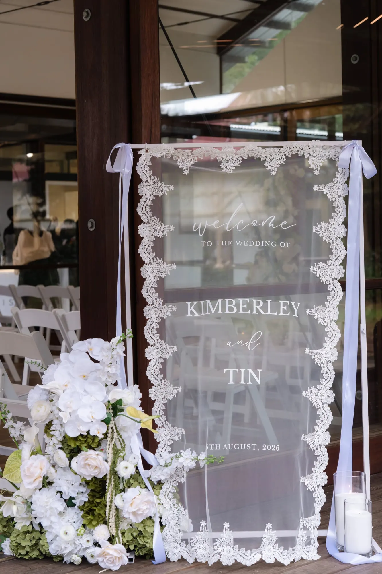 Welcome sign draped in white lace, with white florals at its base
