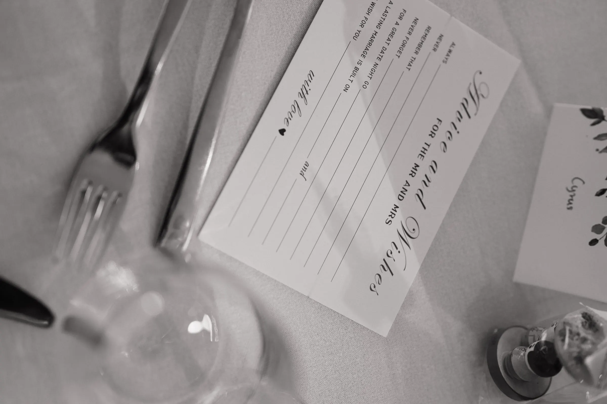 Black-and-white photo of a wishes card beside cutlery on a reception table