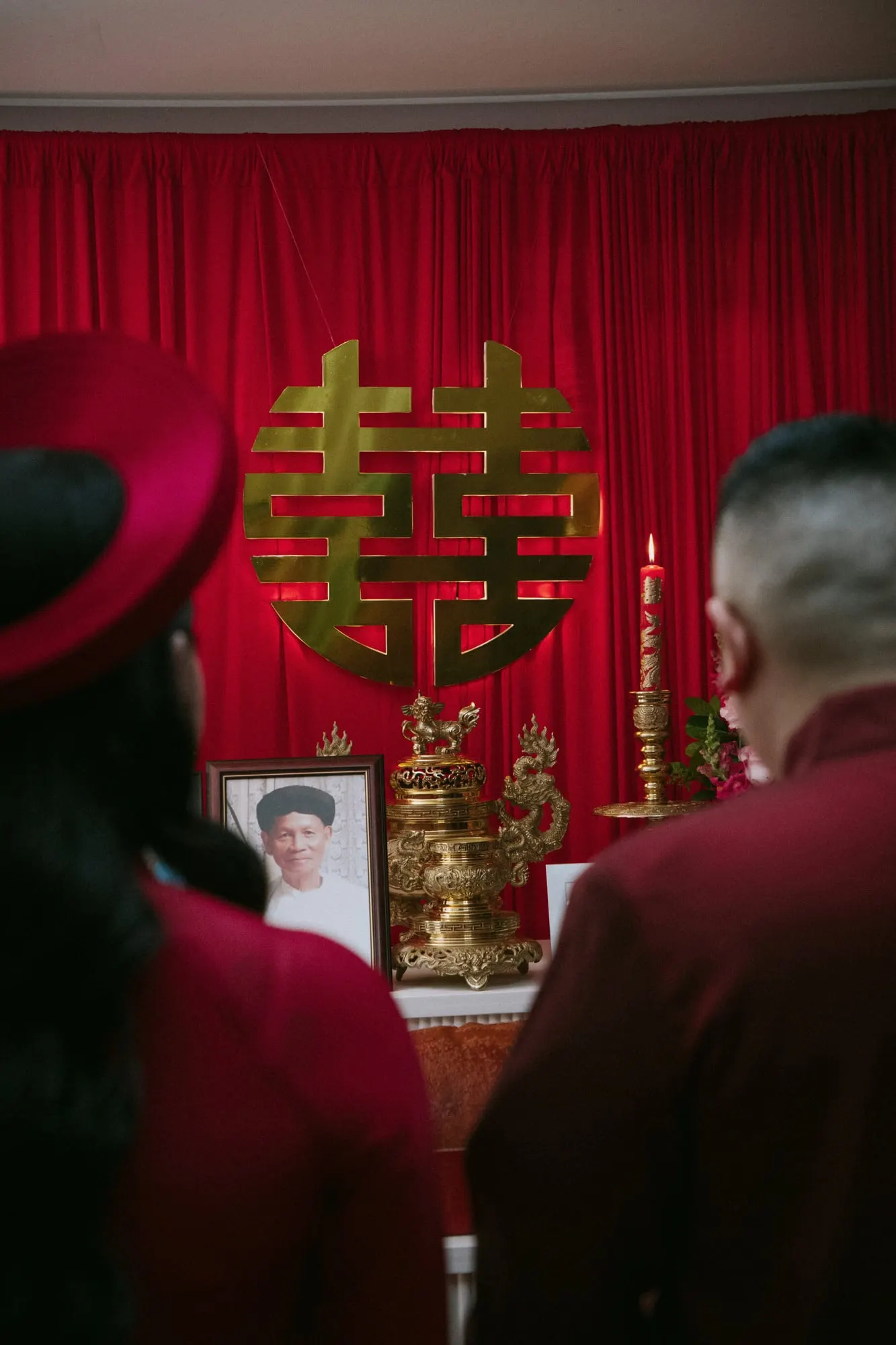 Couple at the altar before a red drape and gold double happiness symbol