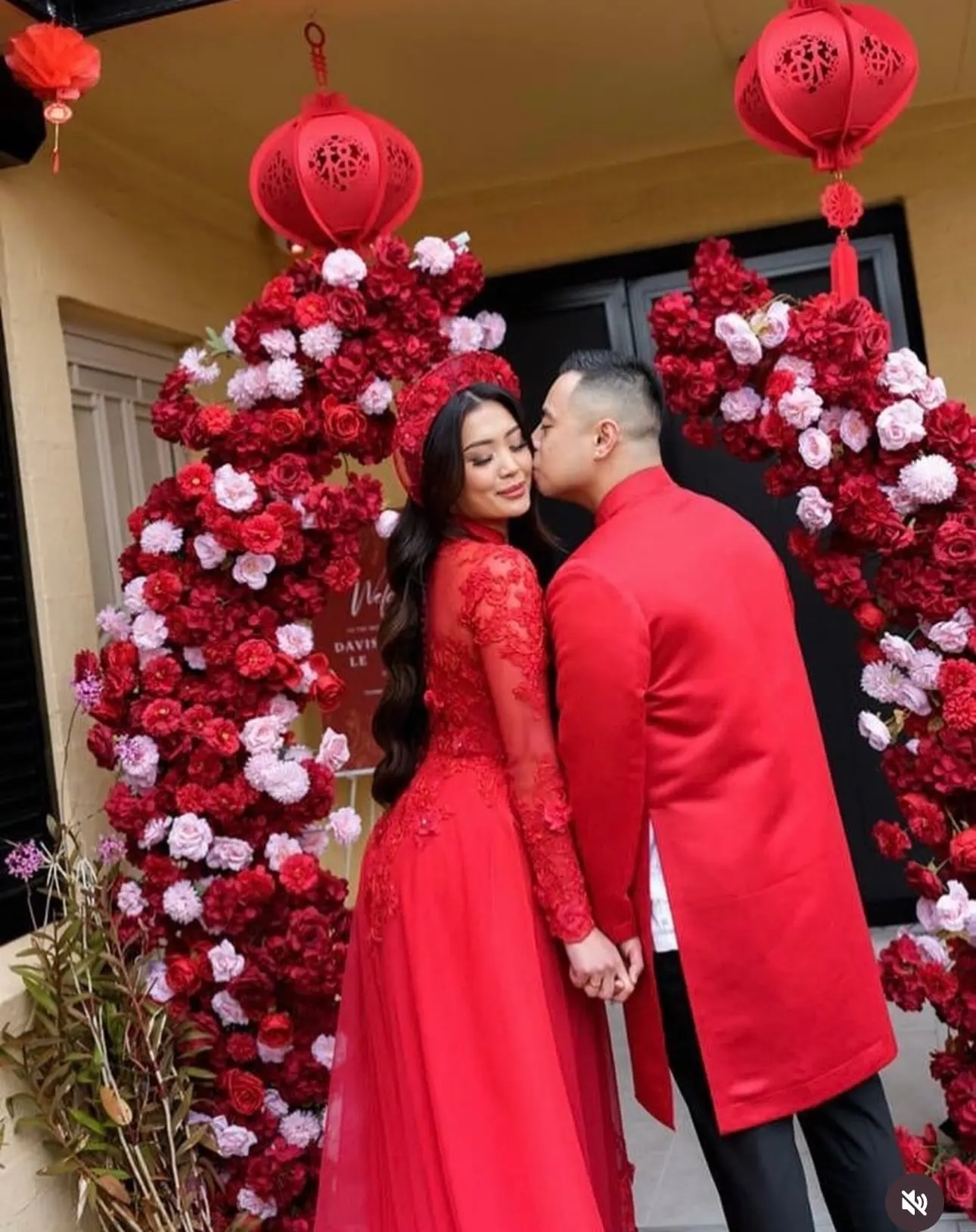 Couple in red traditional dress kissing between red rose columns and lanterns