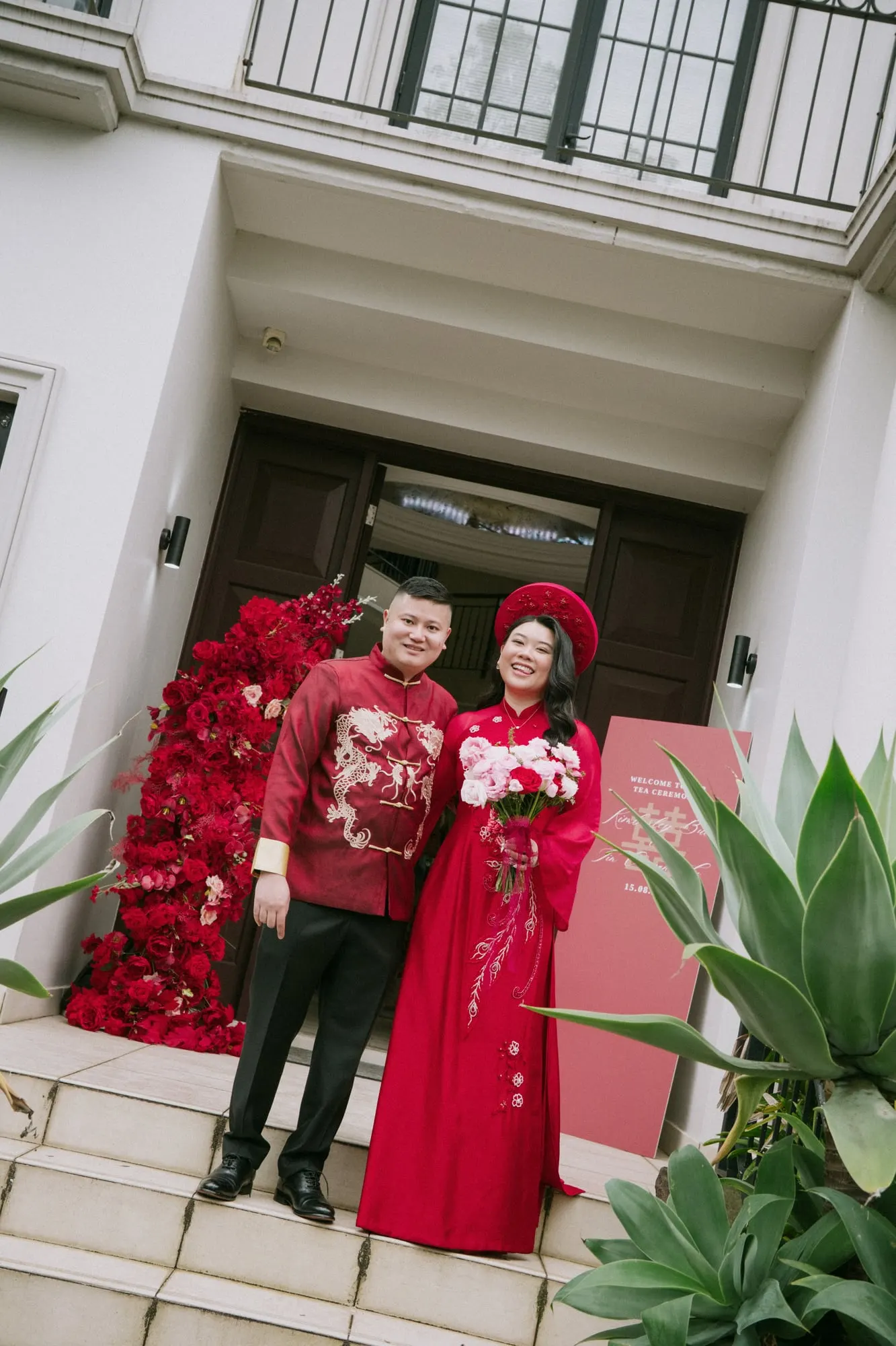 Couple in red on the front steps, between red rose installations