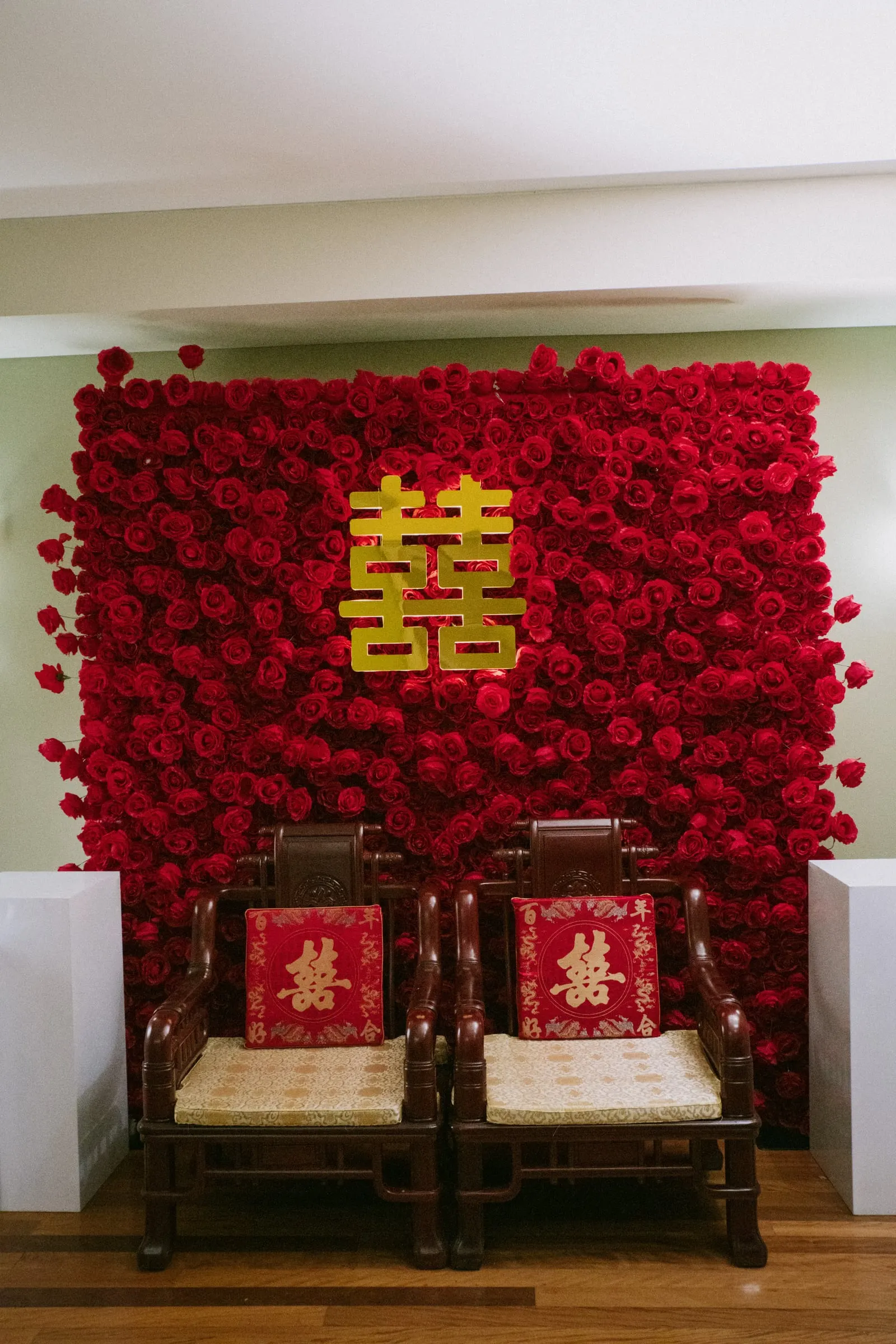 Red rose flower wall with a gold double happiness symbol and two carved chairs